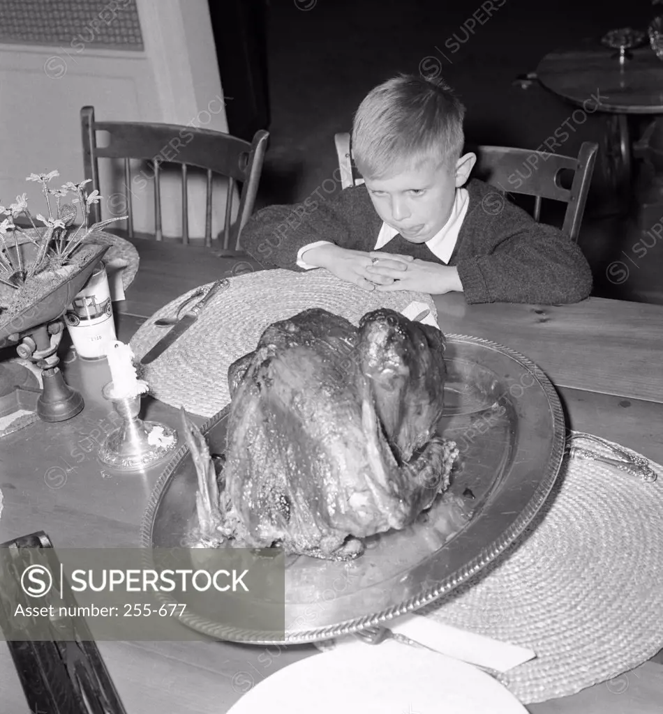 Boy sitting at dining table and looking at roasted turkey on Thanksgiving Day