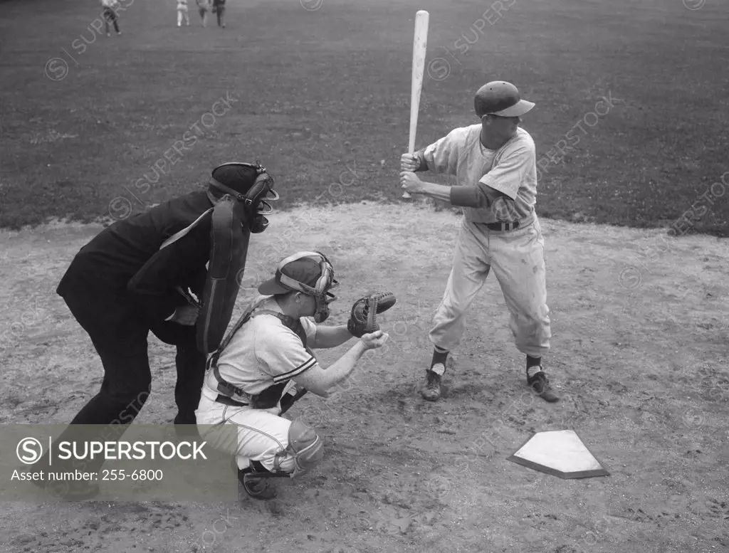 Baseball player swinging a baseball bat with a baseball catcher and a baseball umpire beside him