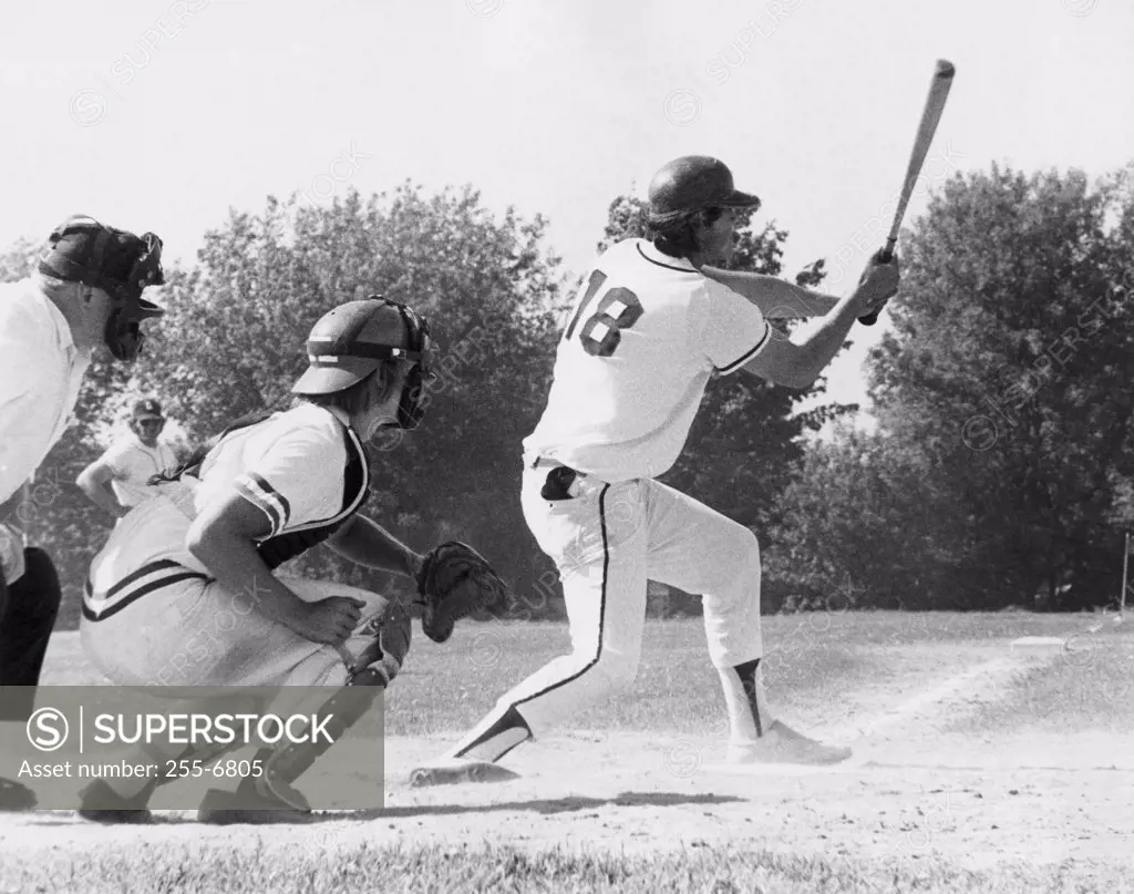 Batter swinging a bat with a catcher and an umpire crouching behind him