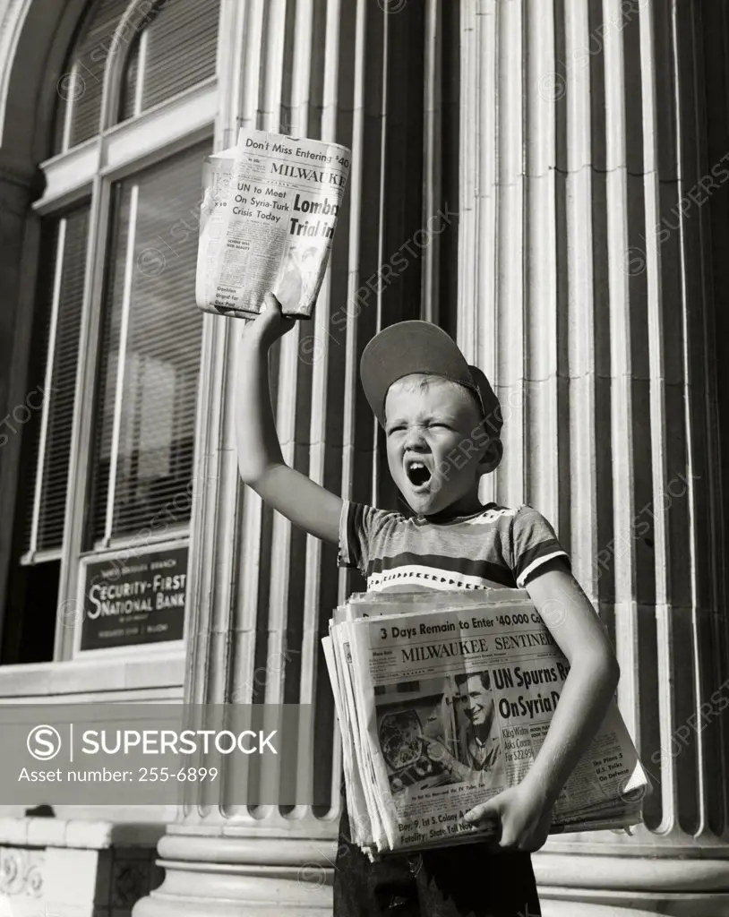 Boy selling newspapers in front of a building