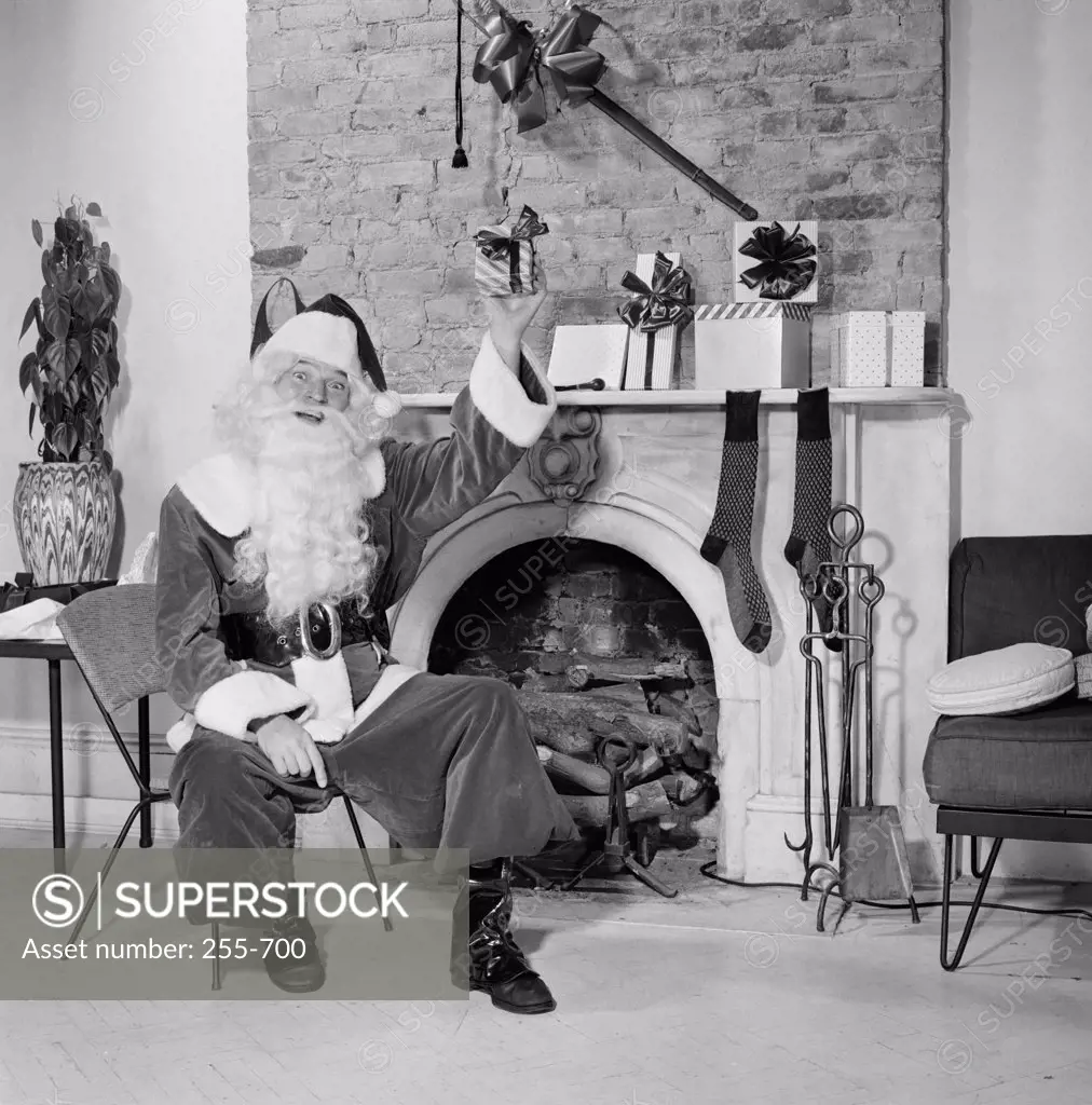 Portrait of Santa Claus sitting in front of a fireplace and holding a Christmas present