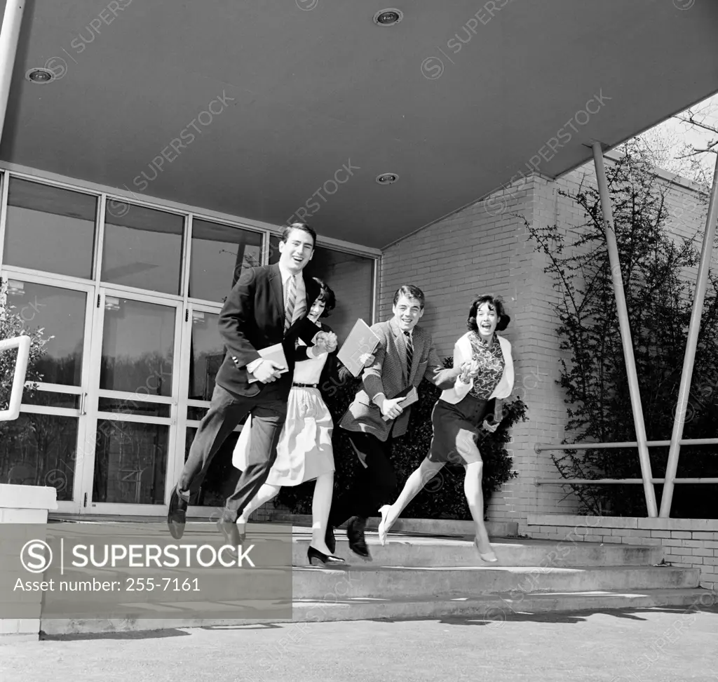 Two young men and two young women running out of a university building