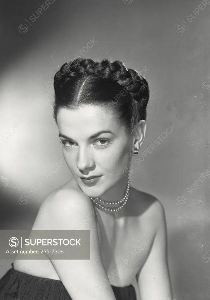 Glamorous woman with dark braided hair wearing pearl necklace and bare shouldered blouse