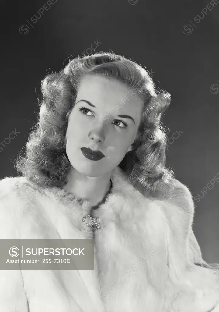 Blonde woman wearing white fur coat looking up at corner