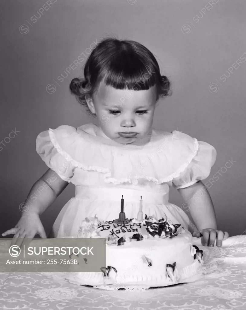 Girl looking at birthday cake, making a face