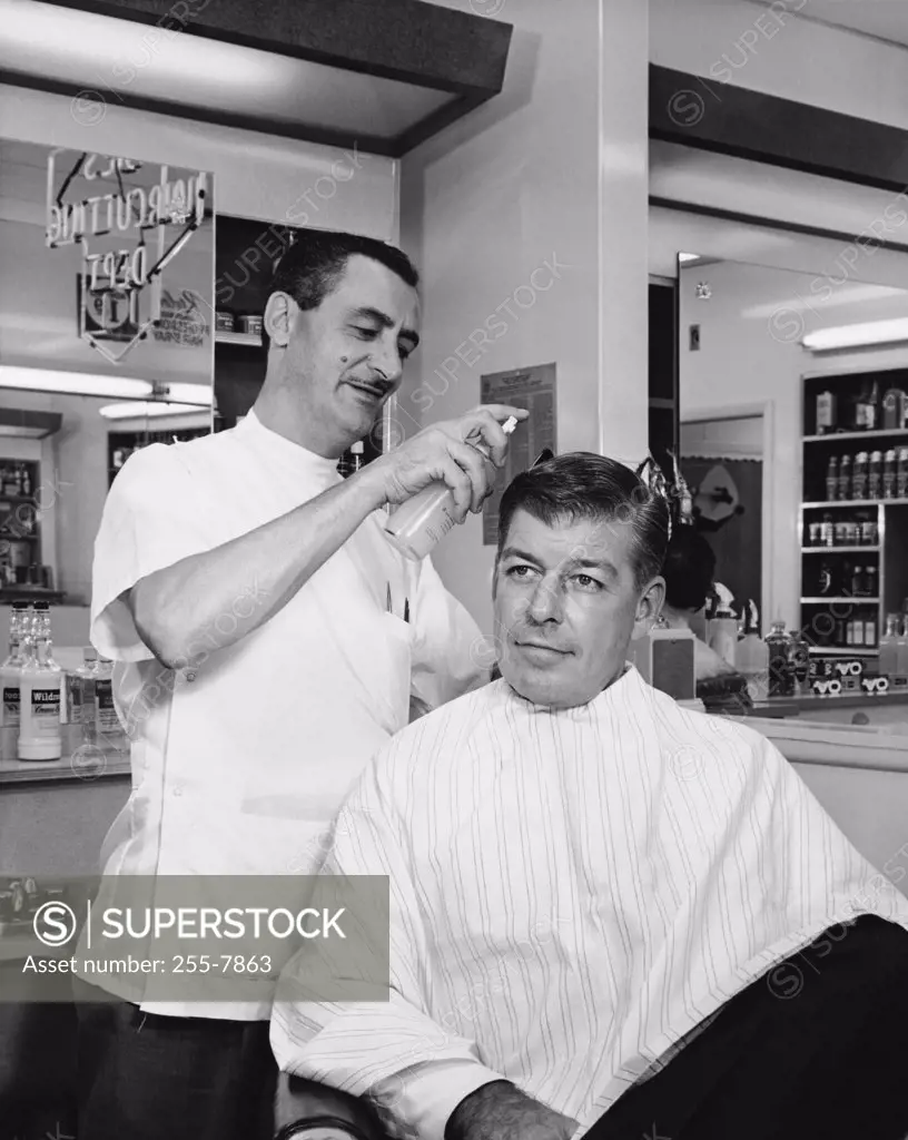Barber spraying hair of a mid adult man in a salon