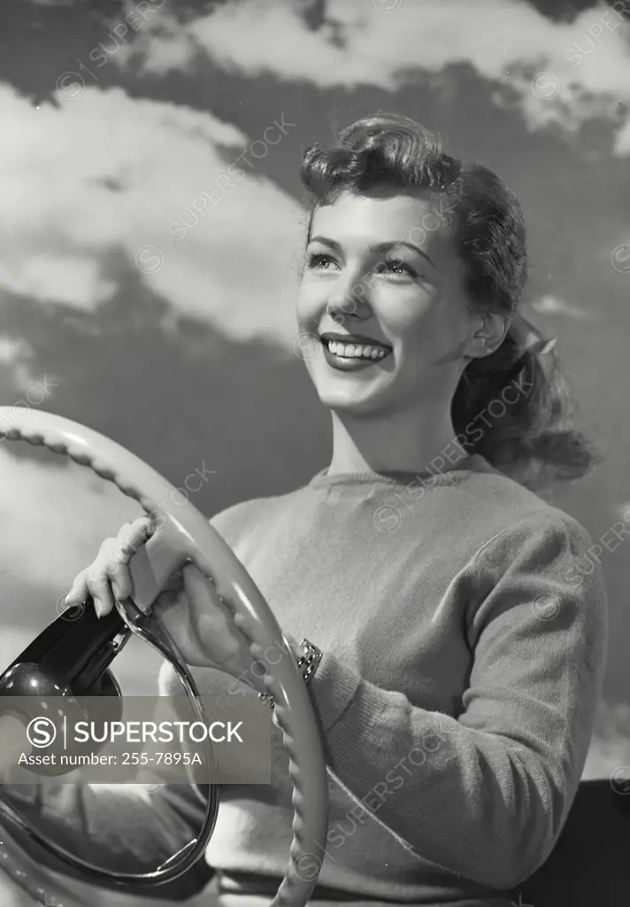 Smiling woman driving car with clouds behind her head