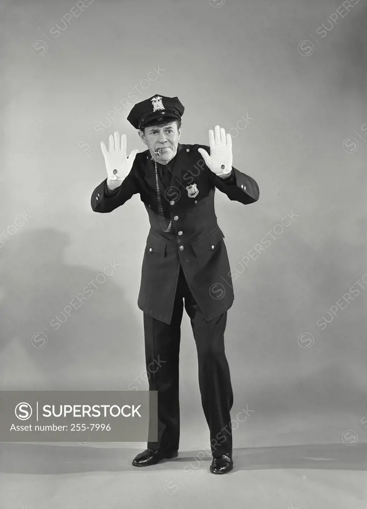 Vintage photograph. Full length portrait of policeman blowing whistle with both hands raised