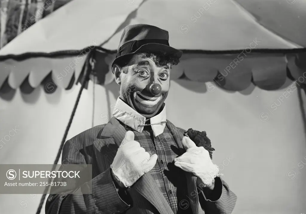 Vintage Photograph. Hobo clown smiling and holding lapels of suit in front of circus tent in background