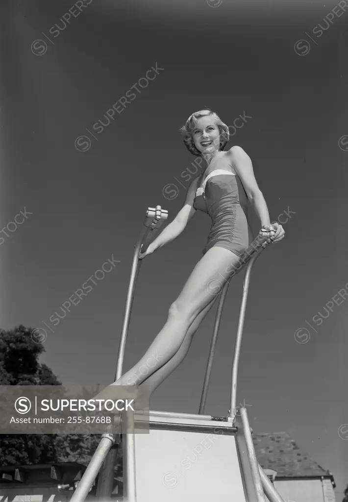 Vintage Photograph. Smiling blonde woman wearing bathing suit standing at top of slide outside, Frame 4