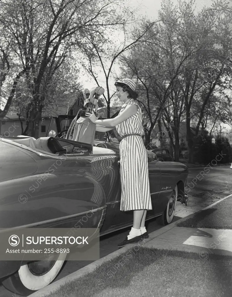 Vintage photograph. Woman putting golf clubs in case into convertible car