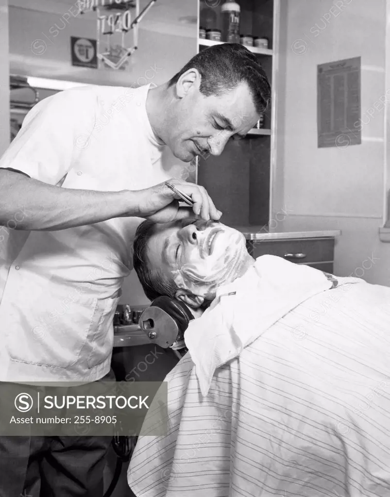 Side profile of a barber shaving a mid adult man in a barbershop