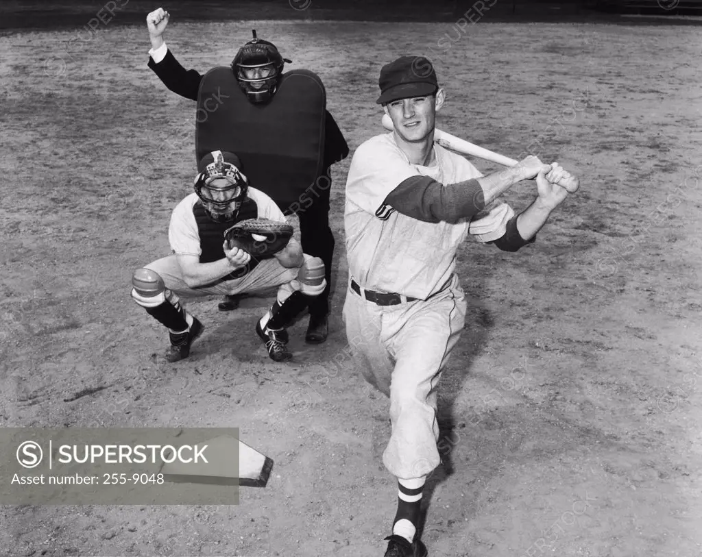 Batter swinging a bat with a catcher and an umpire crouching behind him