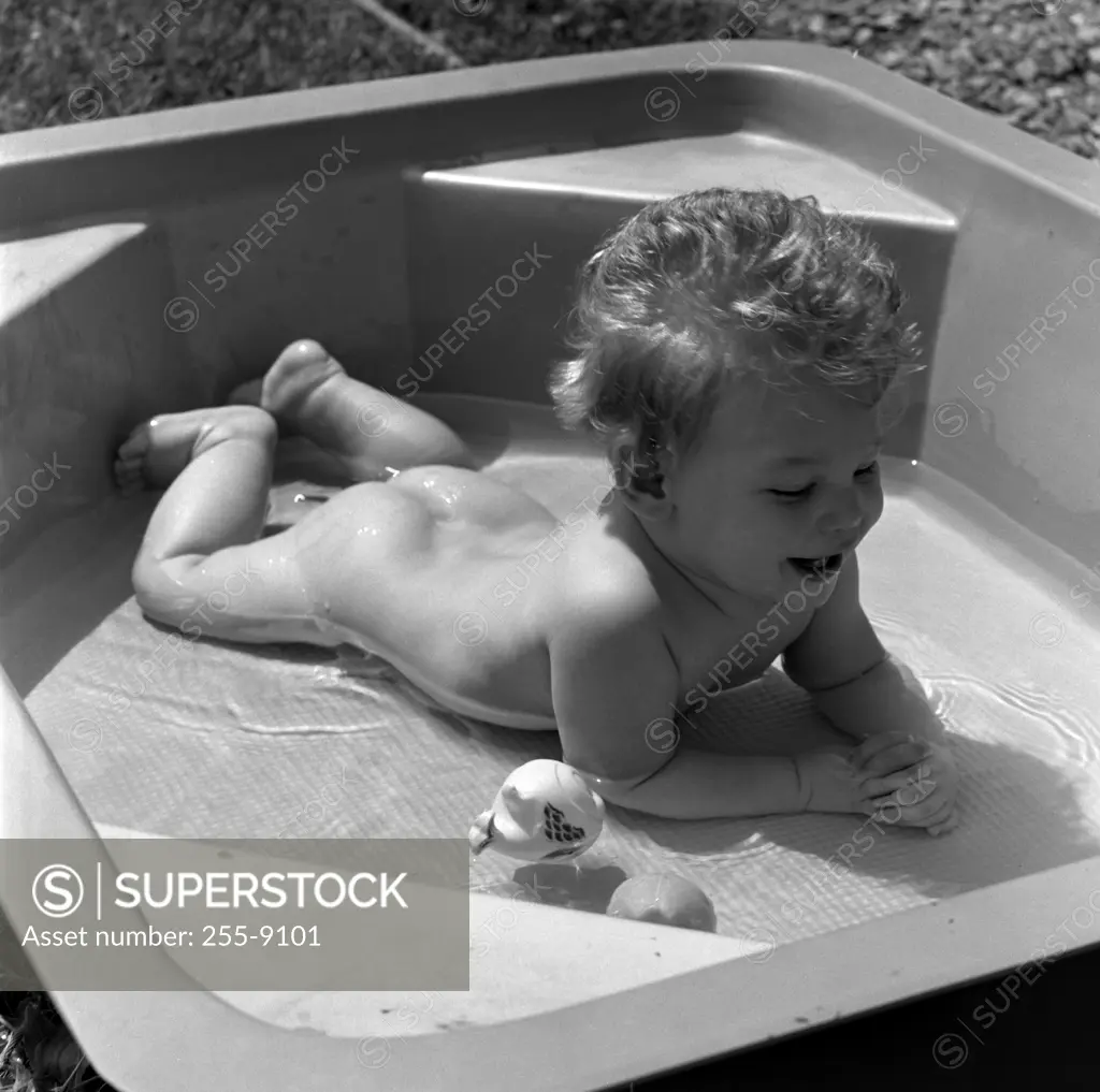 Naked baby lying on front in wading pool