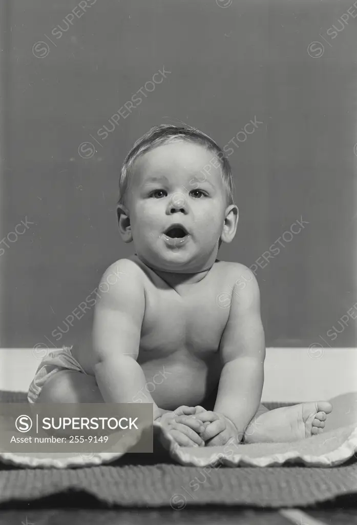 Vintage Photograph. Baby boy looking at camera sitting on thin blanket