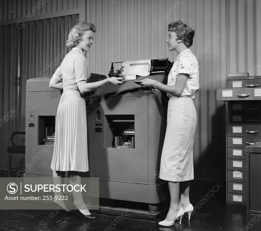 Side profile of two businesswomen standing in front of a machine