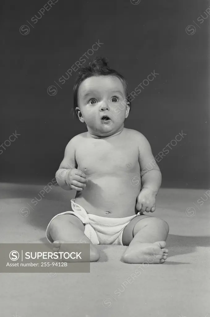 Vintage Photograph. Baby sitting on flat surface with funny shocked expression on face