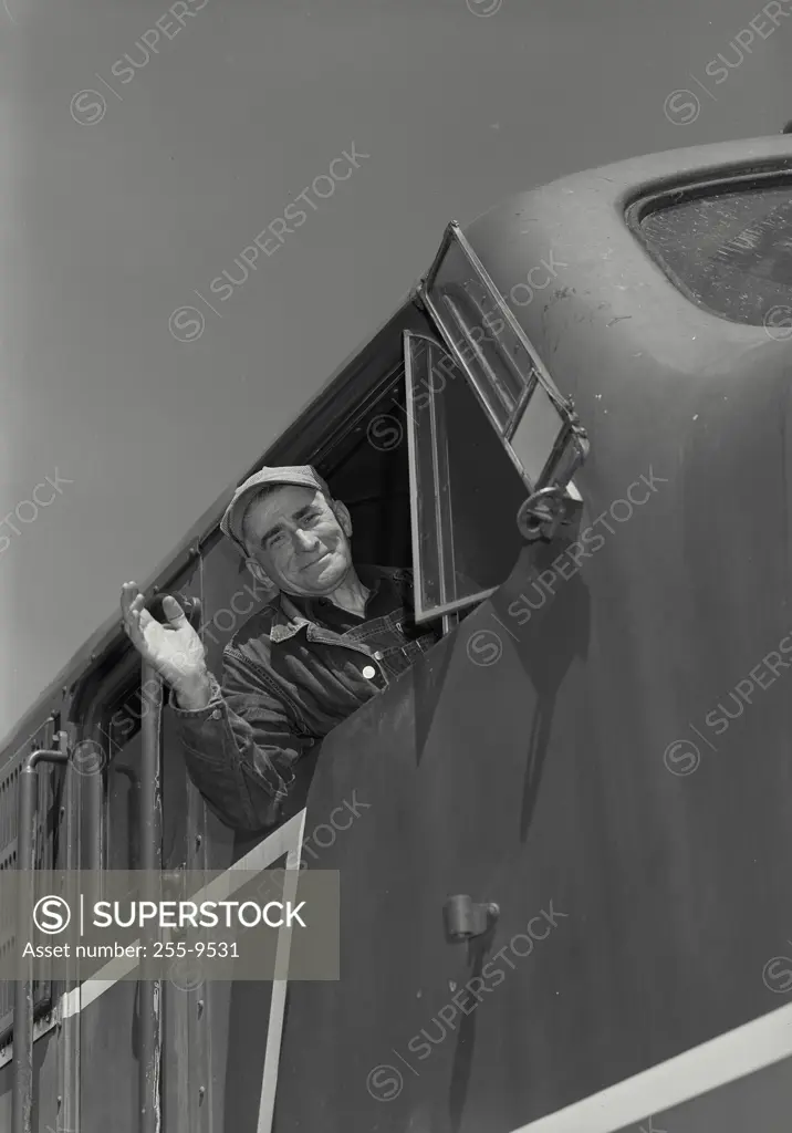 Vintage Photograph. Closeup of Railroad engineer looking out of locomotive cab smiling and waving