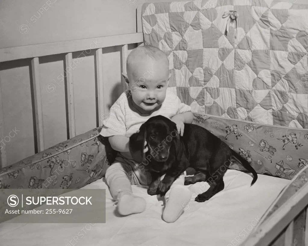 Baby playing with a puppy in a crib