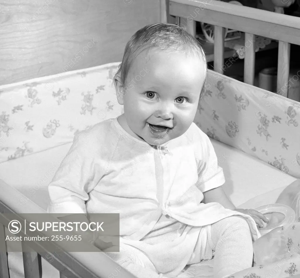 Portrait of cheerful baby sitting in cot