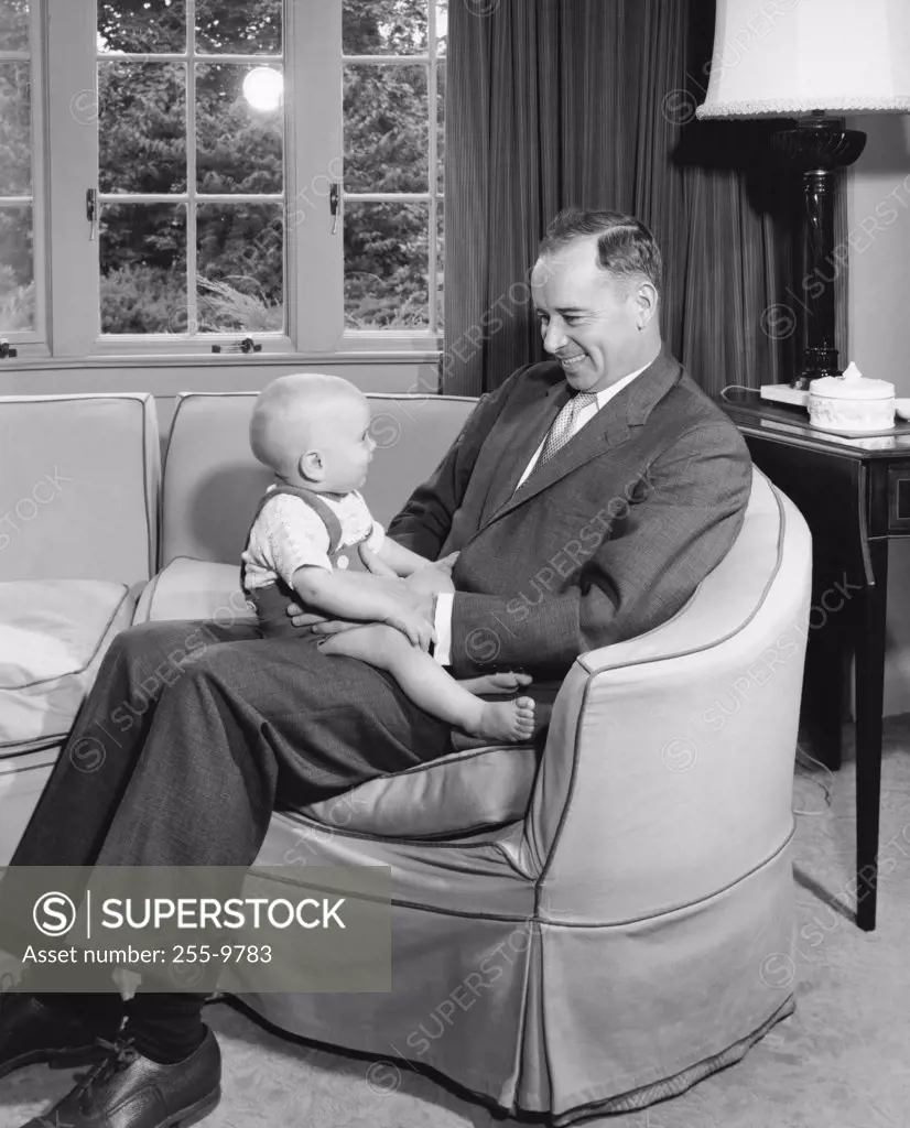 Mid adult man sitting in an armchair holding his son and smiling