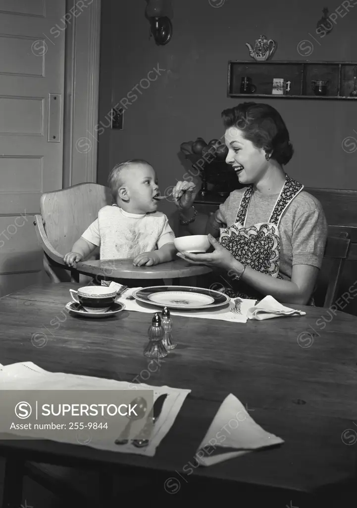 Vintage Photograph. Mother feeding baby in high chair.