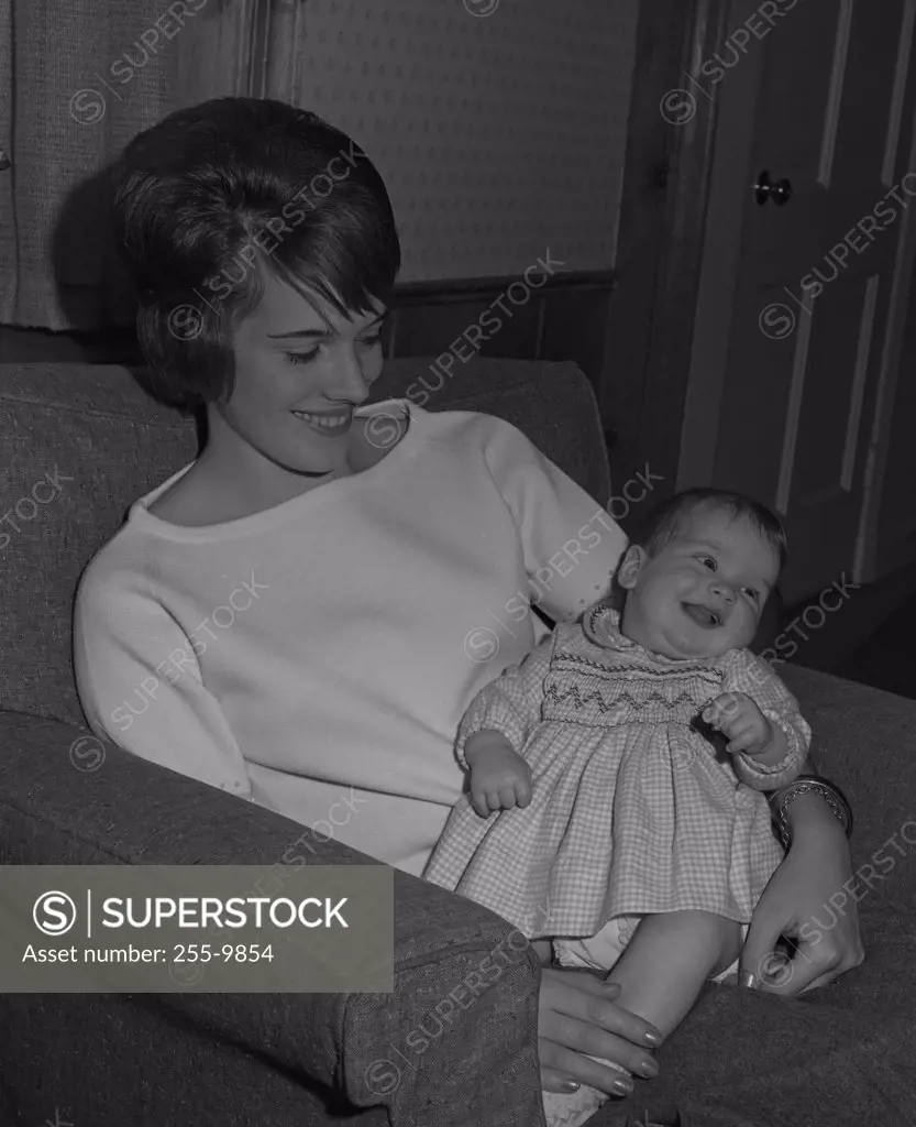 Mother sitting in armchair with baby in arms and smiling