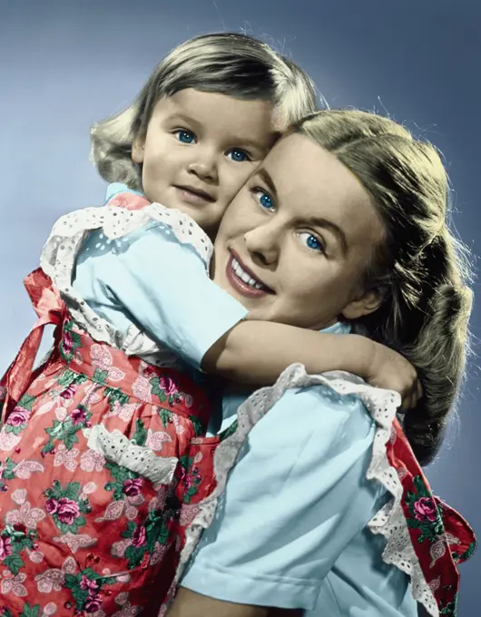 Adorable little girl hugging mother with faces pressed together wearing matching dresses