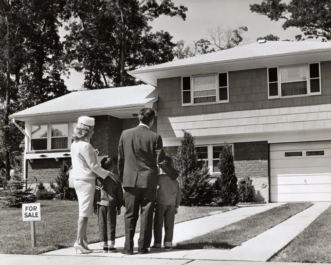 Rear view of parents standing with their two children in front of a house