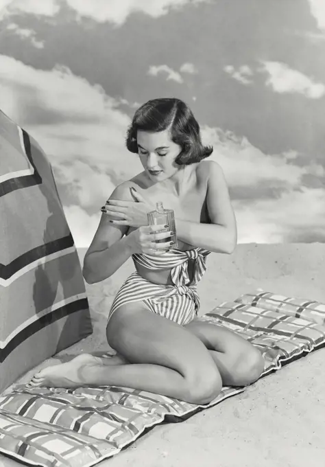 Vintage photograph. Woman in bikini sitting on mat applying tanning oil