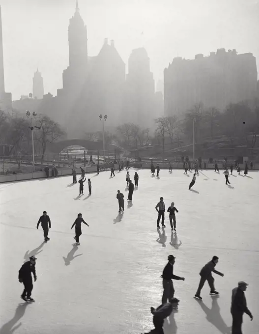 Vintage photograph. People skating at Wollman Memorial Ice Rink in Central Park with hazy buildings in background