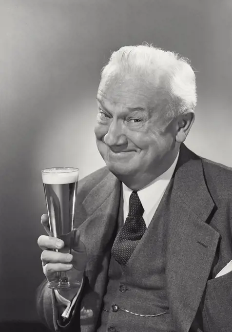 Vintage photograph. Elderly white haired gentleman holding up glass of beer grinning