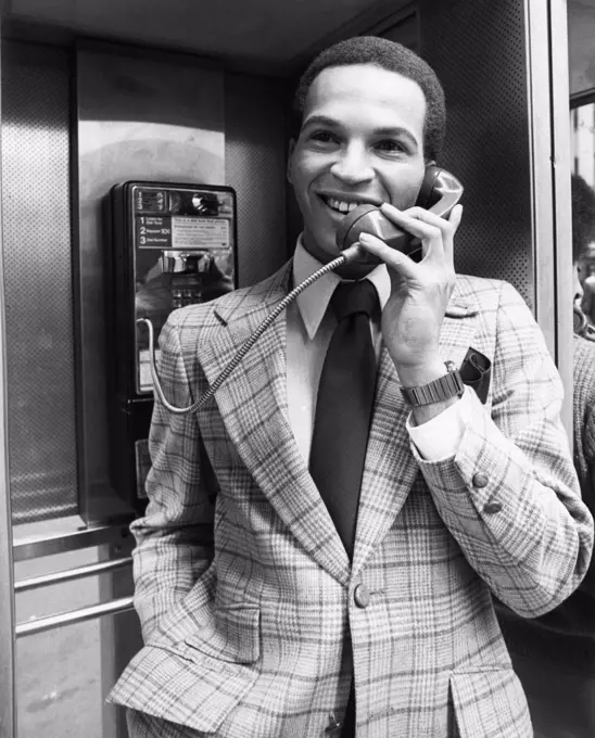 Young man wearing suit talking in telephone booth