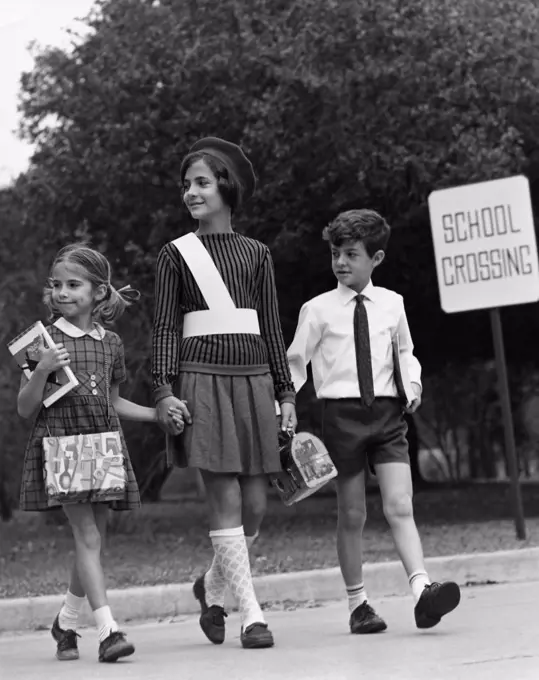 Female crossing guard assisting a boy and girl at road crossing