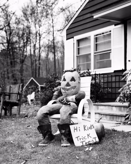 Scarecrow in a Halloween costume sitting in an armchair in front of a house