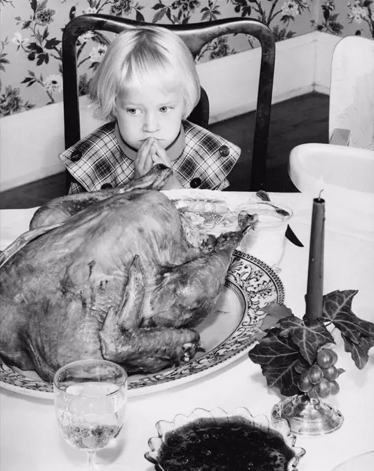 High angle view of a girl sitting at a dining table and looking at a roast turkey on Thanksgiving Day