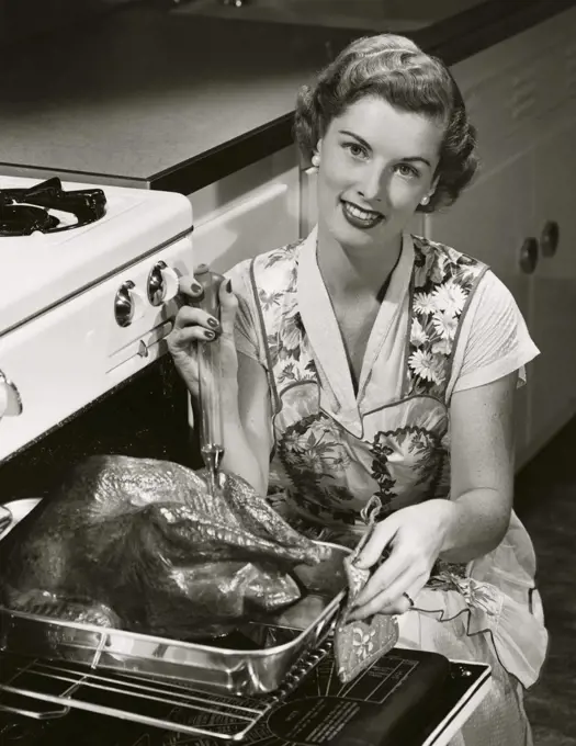 Portrait of a young woman putting a turkey into an oven