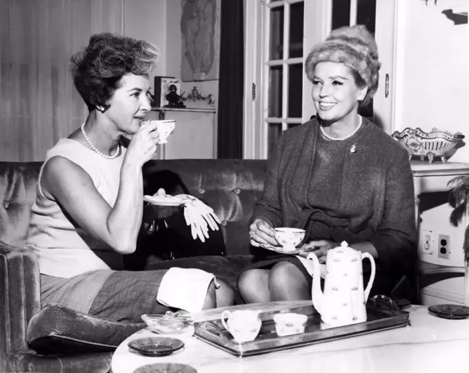 Two women drinking tea and talking in living room