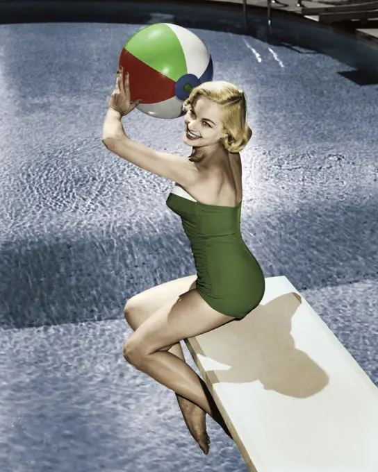 Side profile of young woman sitting on diving board holding beach ball