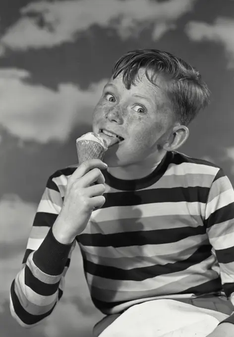 Vintage photograph. Young boy in striped shirt licking ice cream cone looking at camera