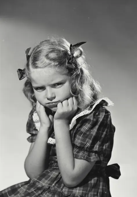Vintage Photograph. Young girl making pouty expression with hands on chin