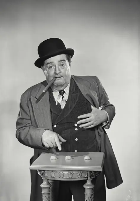 Vintage Photograph. Street gambler with cigar in mouth pointing at  shells of nuts for game and patting pockets