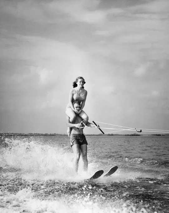 Young man waterskiing in sea with young woman sitting on his shoulders
