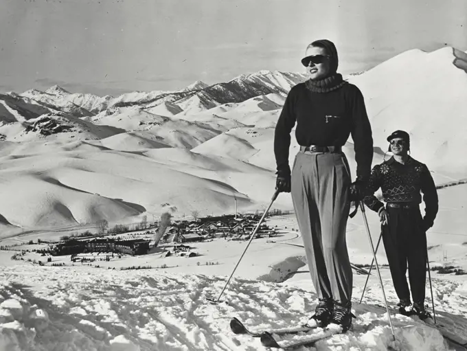 Vintage photograph. Skiing couple with view of Sun Valley from atop Dollar Mountain with jagged Sawtooth mountains in the background