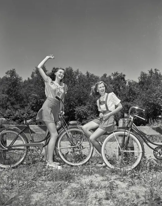 Vintage Photograph. Girls sitting on bicycles in field together waving