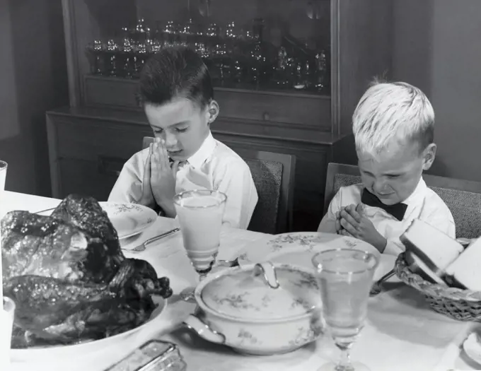 Two boys praying at a dining table on Thanksgiving Day