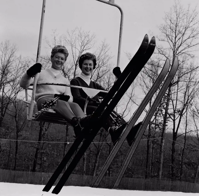 Two woman sitting ski lift, looking at camera and smiling