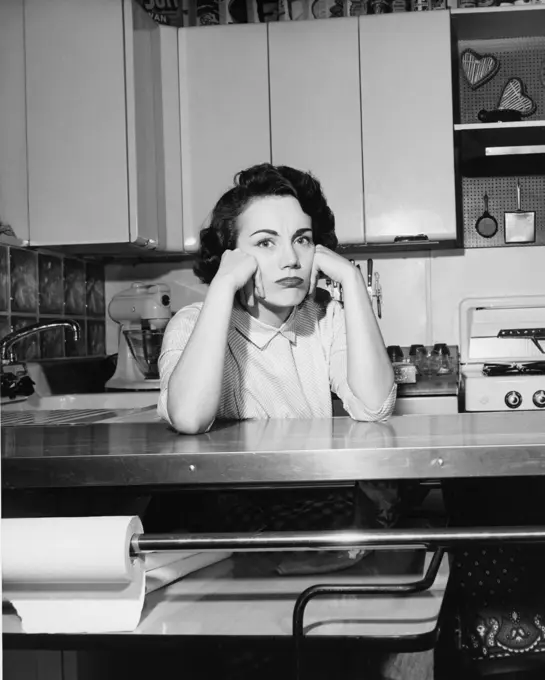 Portrait of a young woman sitting in the kitchen thinking