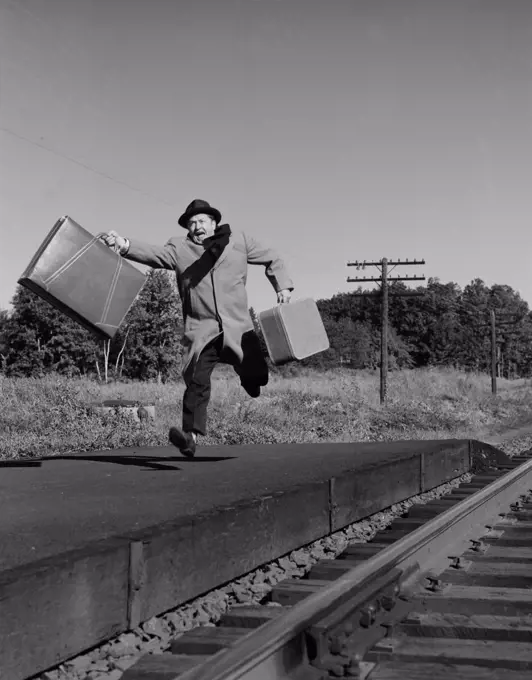 Man with suitcases running along railroad track