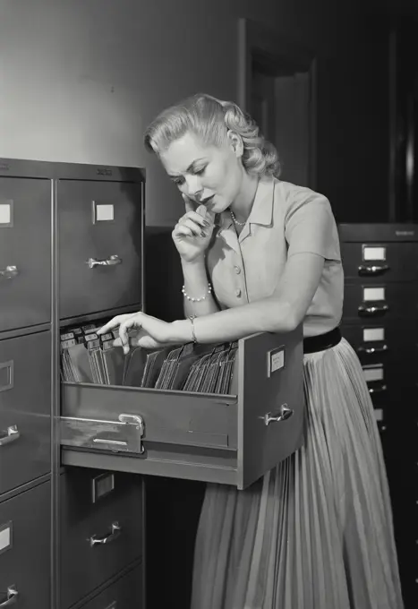 Vintage Photograph. Young woman wearing dress going through folders in drawer of filing cabinet, Frame 4